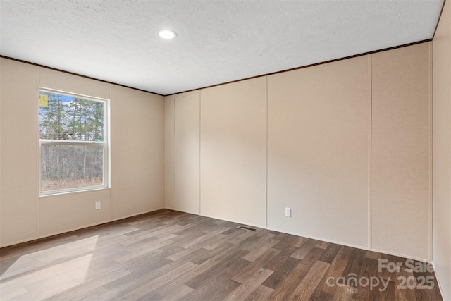 unfurnished room with a textured ceiling, visible vents, and wood finished floors