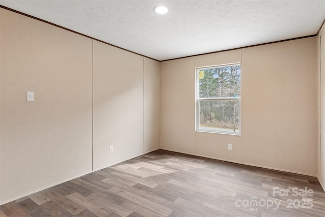 empty room featuring light wood-style flooring, ornamental molding, and a textured ceiling