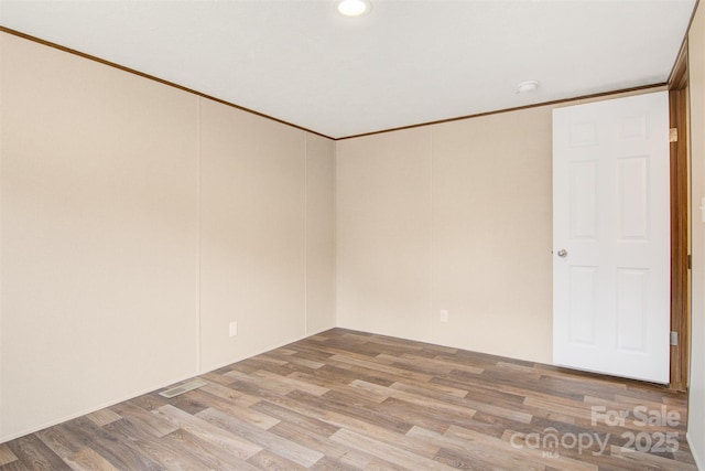 empty room featuring ornamental molding, light wood-type flooring, and visible vents