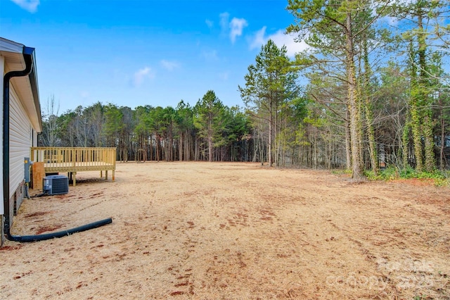 view of yard with central AC, a view of trees, and a wooden deck