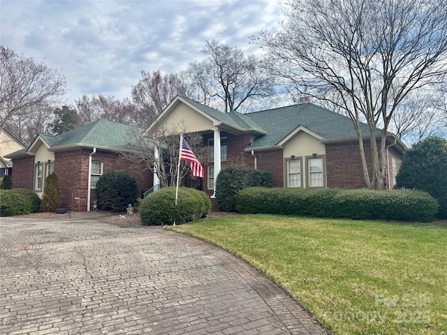 view of front of property featuring a shingled roof, decorative driveway, brick siding, and a front lawn