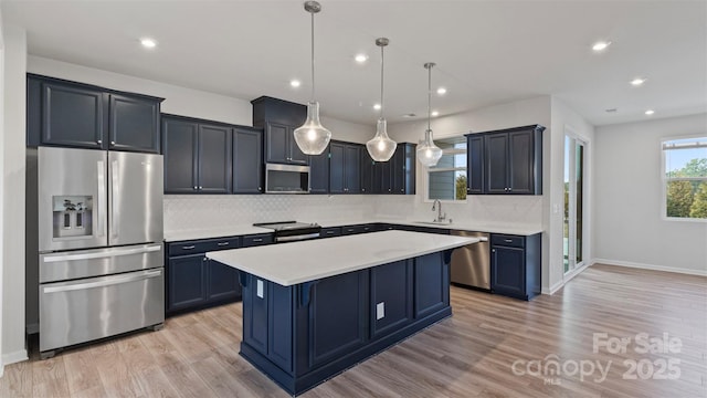 kitchen with decorative light fixtures, a center island, stainless steel appliances, light countertops, and a sink