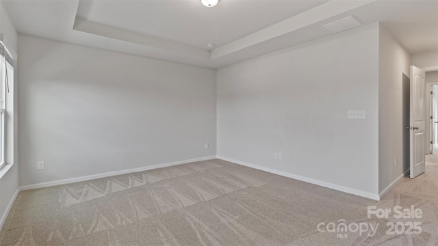 unfurnished room featuring baseboards, a tray ceiling, visible vents, and light colored carpet