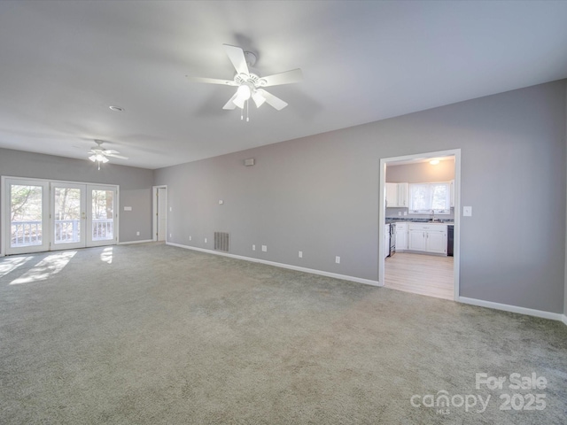 unfurnished living room with light colored carpet, visible vents, a ceiling fan, a healthy amount of sunlight, and baseboards