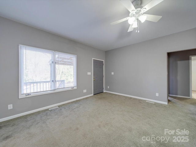 carpeted empty room featuring ceiling fan, visible vents, and baseboards