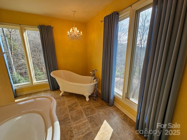 bathroom with baseboards, a soaking tub, an inviting chandelier, and a healthy amount of sunlight