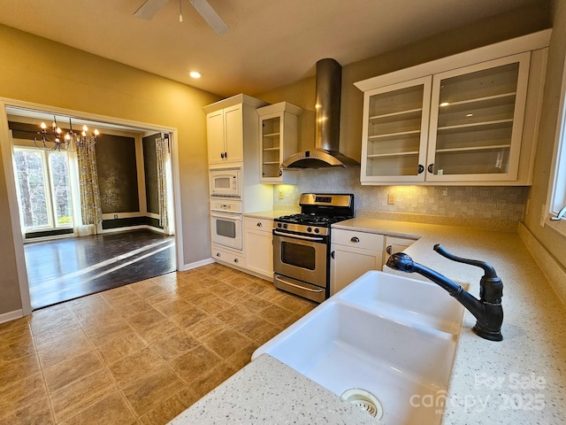 kitchen with white appliances, wall chimney exhaust hood, glass insert cabinets, and light countertops