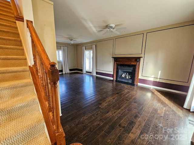 unfurnished living room with ceiling fan, a decorative wall, a fireplace, wood finished floors, and stairway