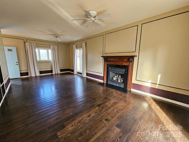 unfurnished living room featuring a fireplace with flush hearth, dark wood finished floors, a decorative wall, and a ceiling fan