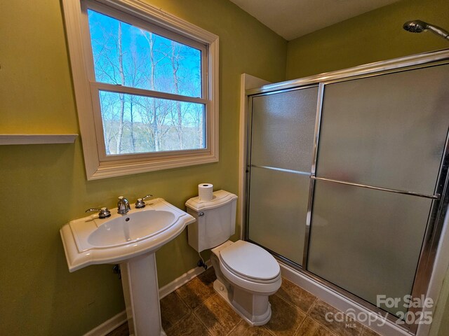 bathroom with toilet, a stall shower, and baseboards