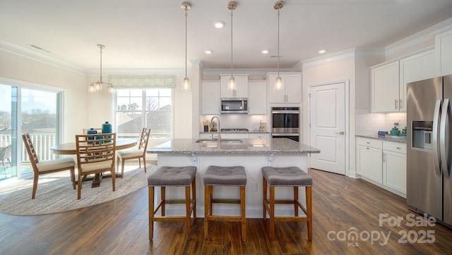 kitchen with a kitchen island with sink, white cabinets, appliances with stainless steel finishes, light stone countertops, and decorative light fixtures