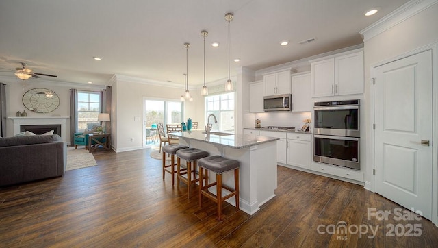 kitchen with appliances with stainless steel finishes, open floor plan, white cabinets, and a center island with sink