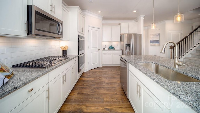 kitchen with light stone counters, stainless steel appliances, a sink, white cabinets, and pendant lighting