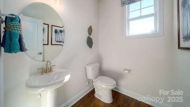 half bath with baseboards, a sink, toilet, and wood finished floors