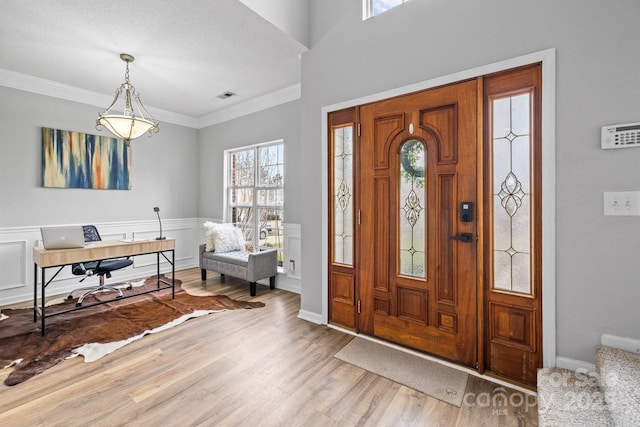 foyer with visible vents, crown molding, wainscoting, wood finished floors, and a decorative wall