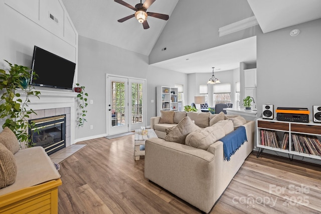 living room with visible vents, a tiled fireplace, ceiling fan with notable chandelier, wood finished floors, and high vaulted ceiling