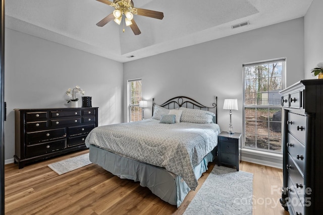 bedroom featuring ceiling fan, visible vents, multiple windows, and wood finished floors