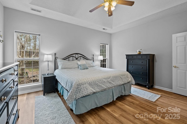 bedroom featuring visible vents, a raised ceiling, baseboards, and wood finished floors