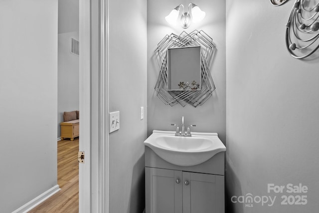 bathroom with visible vents, vanity, baseboards, and wood finished floors