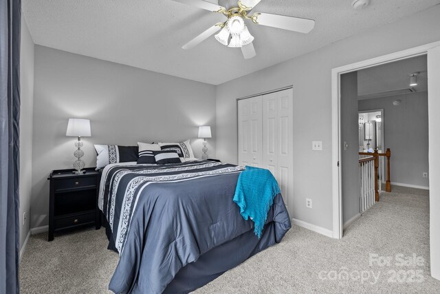 carpeted bedroom with baseboards, attic access, a closet, a textured ceiling, and a ceiling fan