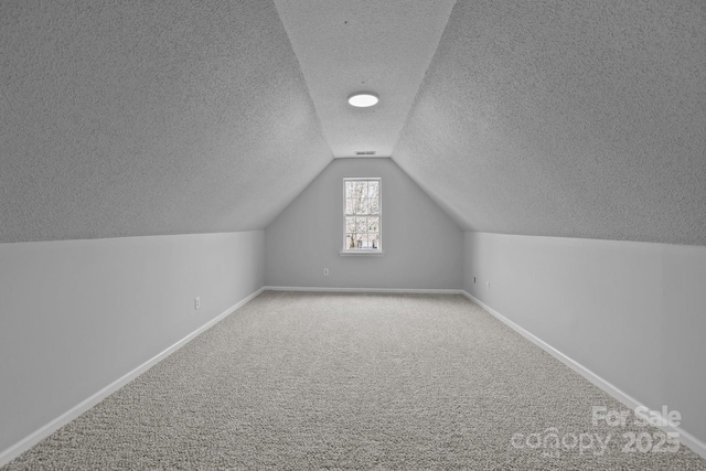 additional living space featuring carpet, baseboards, visible vents, vaulted ceiling, and a textured ceiling