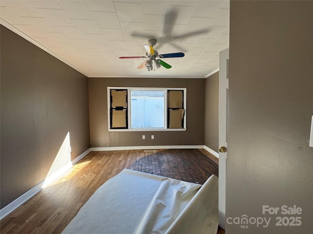 empty room featuring ceiling fan, crown molding, baseboards, and wood finished floors