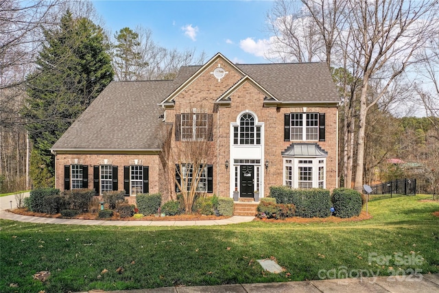 view of front of home featuring a shingled roof, a front lawn, and brick siding