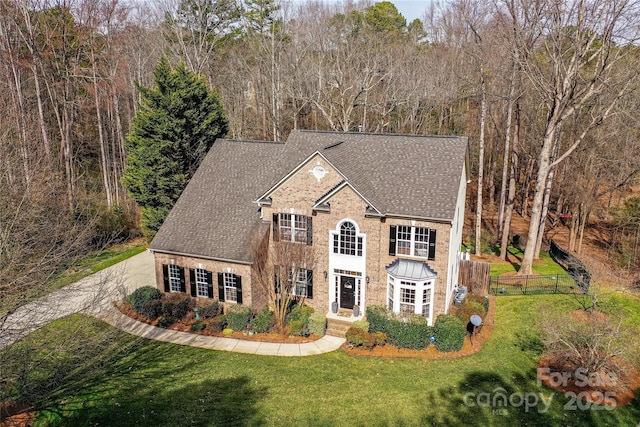 view of front of property featuring a shingled roof, a front yard, brick siding, and fence