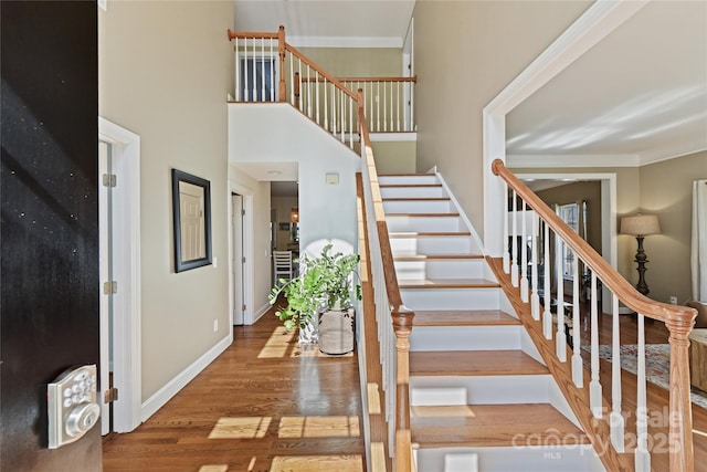 stairs featuring baseboards, a high ceiling, ornamental molding, and wood finished floors