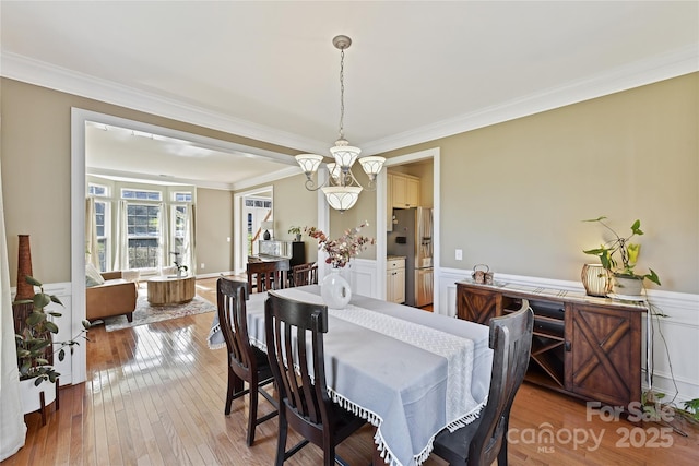 dining room featuring wainscoting, ornamental molding, wood-type flooring, and a notable chandelier