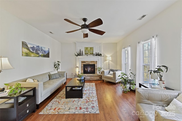 living room featuring a ceiling fan, visible vents, wood finished floors, and a stone fireplace