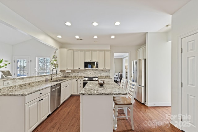 kitchen with tasteful backsplash, a kitchen island, appliances with stainless steel finishes, a kitchen bar, and a sink