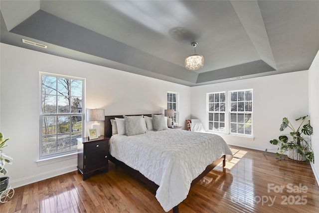 bedroom featuring hardwood / wood-style flooring, visible vents, baseboards, and a raised ceiling