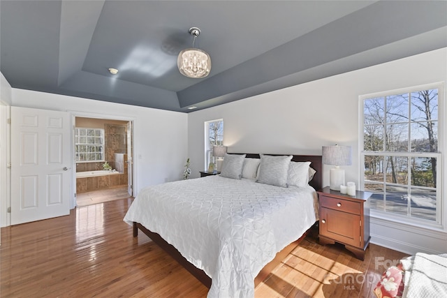 bedroom with a raised ceiling, connected bathroom, an inviting chandelier, and wood finished floors