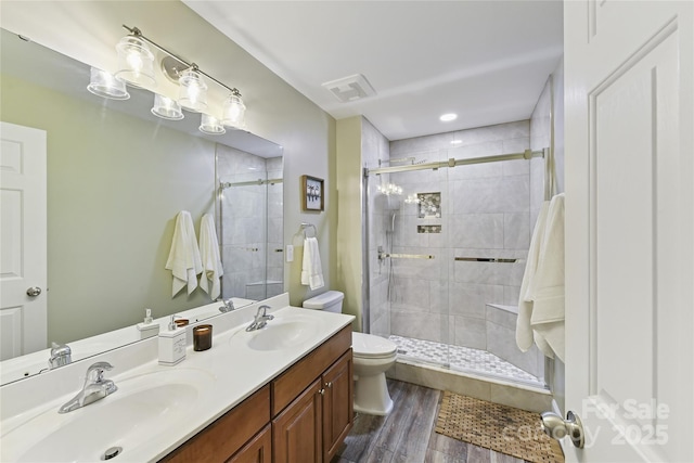 bathroom featuring toilet, a stall shower, a sink, and visible vents