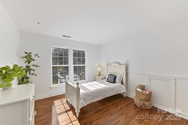 bedroom featuring a wainscoted wall, visible vents, and wood finished floors