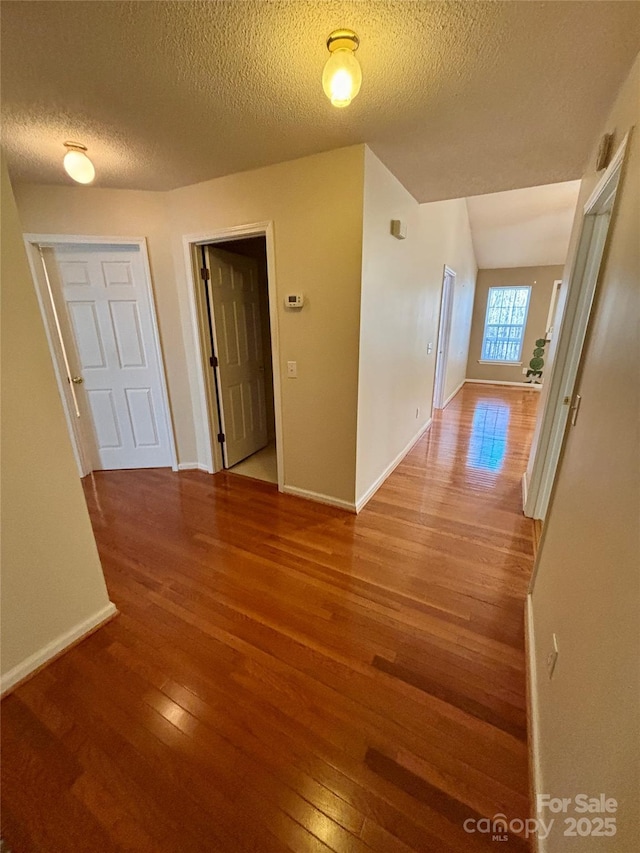 hallway featuring a textured ceiling, baseboards, and wood finished floors