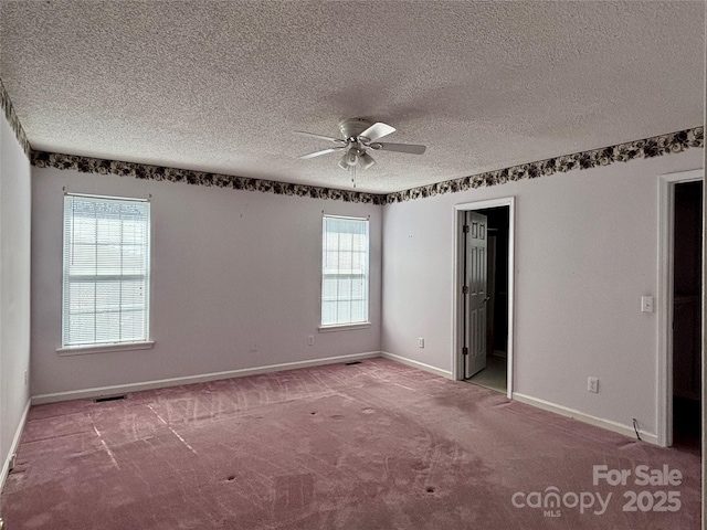 carpeted empty room with visible vents, a textured ceiling, a ceiling fan, and baseboards