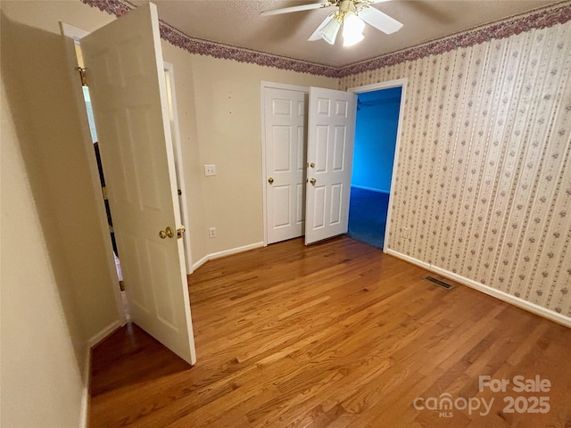 unfurnished bedroom with wallpapered walls, visible vents, baseboards, ceiling fan, and wood finished floors