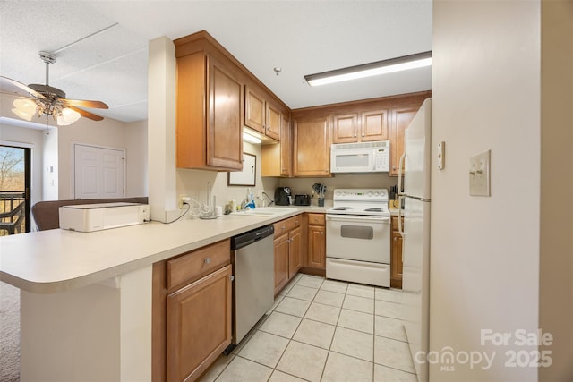 kitchen with light tile patterned floors, a peninsula, white appliances, a sink, and light countertops