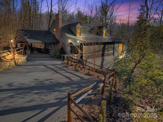 property exterior at dusk with a chimney and aphalt driveway