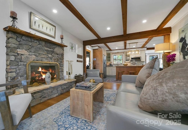 living area featuring recessed lighting, beam ceiling, wood finished floors, and a stone fireplace