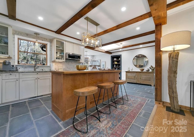 kitchen with stainless steel microwave, a kitchen island, backsplash, beamed ceiling, and glass insert cabinets