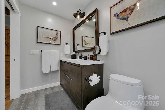 half bathroom with toilet, recessed lighting, wood finished floors, vanity, and baseboards