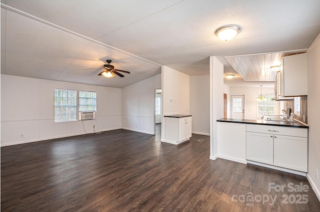 unfurnished living room with baseboards, dark wood finished floors, ceiling fan, cooling unit, and a sink