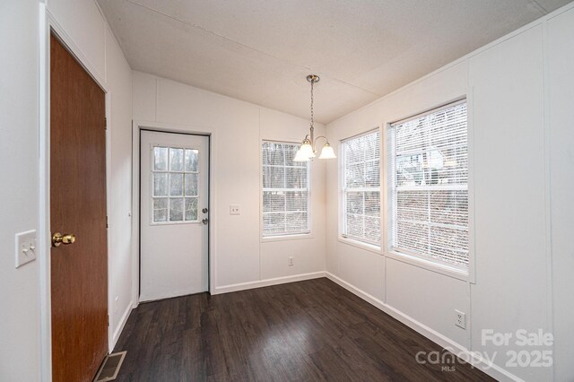 unfurnished dining area with visible vents, dark wood-type flooring, vaulted ceiling, a chandelier, and baseboards