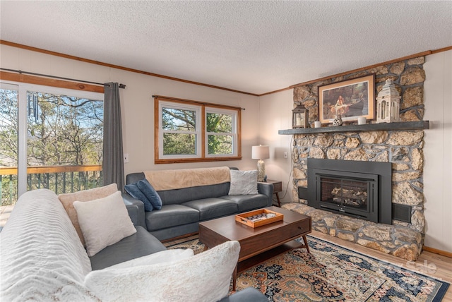 living area with a textured ceiling, wood finished floors, crown molding, and a stone fireplace