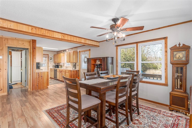 dining room with light wood finished floors, ceiling fan, baseboards, and crown molding