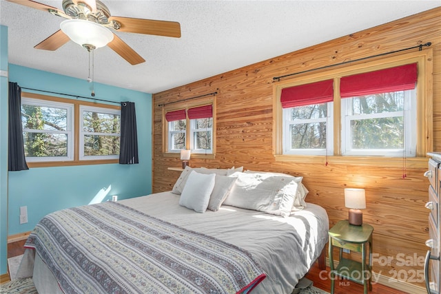 bedroom featuring a ceiling fan, a textured ceiling, and wooden walls