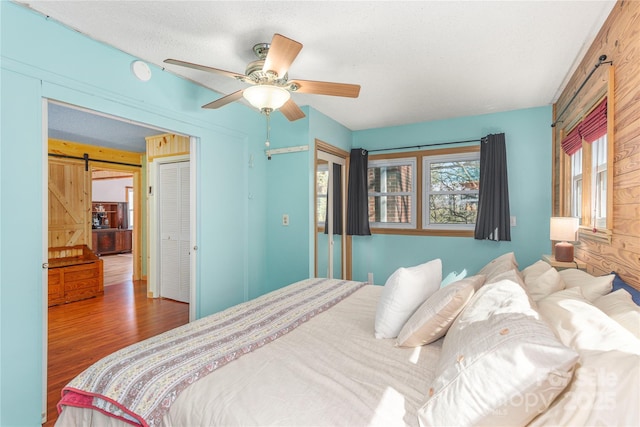 bedroom featuring wood finished floors, ceiling fan, and a barn door